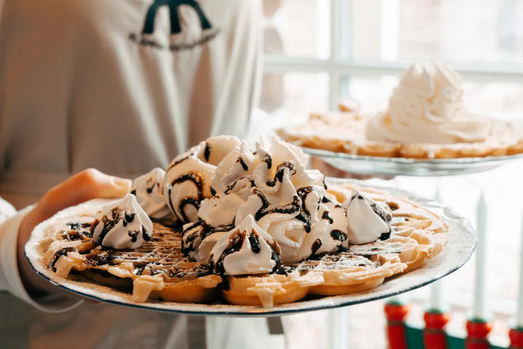 En servitris bär ut två tallrikar med våfflor.