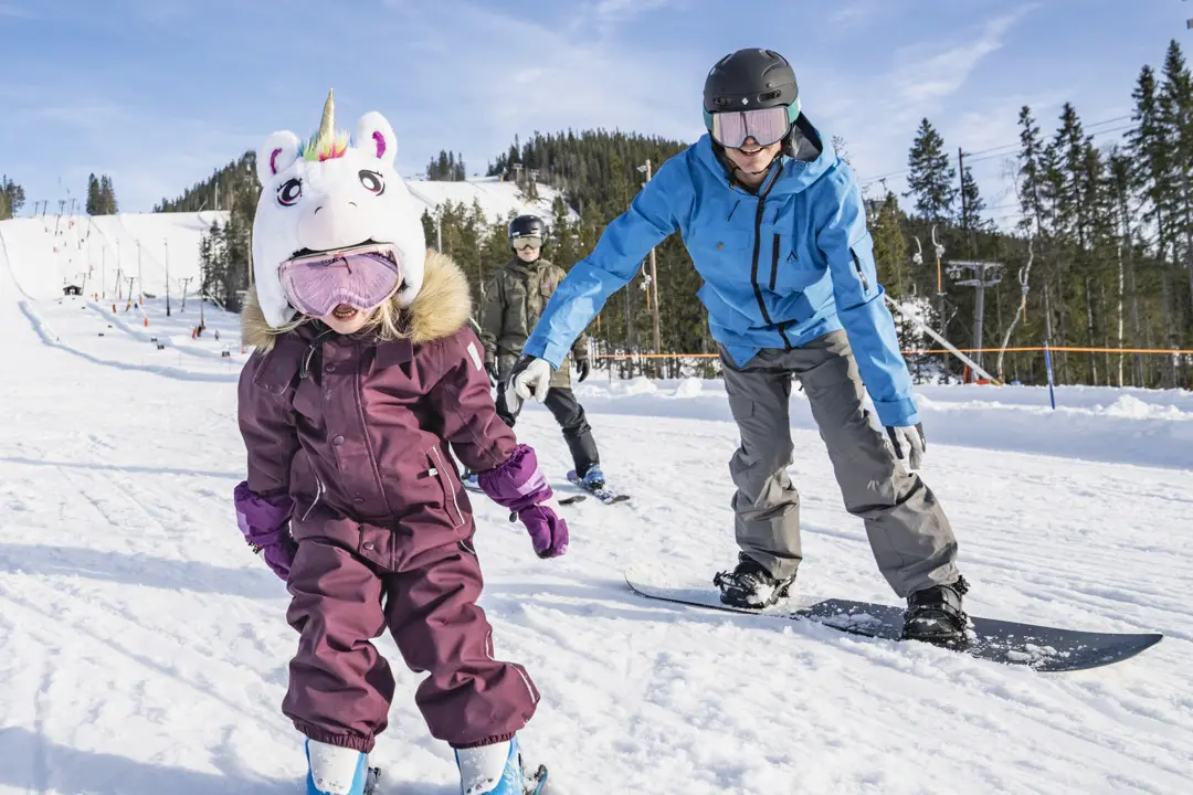 En pappa är ute och svänger i skidbacken tillsammans med dottern i backen.