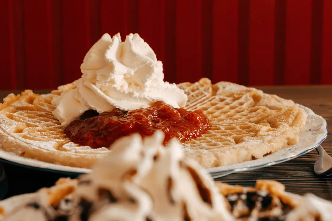 En bild på nygräddade våfflor med jordgubbssylt och grädde