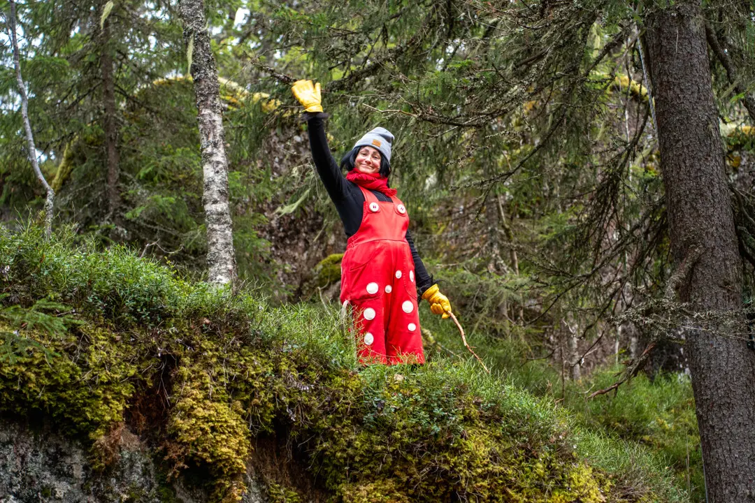 A radiant and cheerful Trolla stands in the ancient forest waving at the camera.