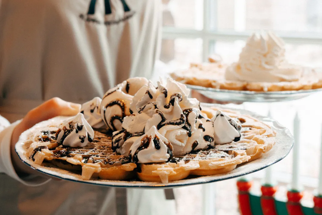 En bild på två våfflor toppad med grädde, maränger och chokladsås