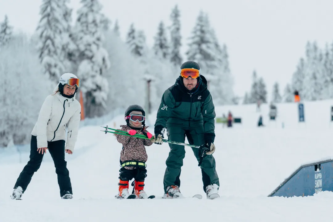 En familj åker skidor på toppen av en snötäckt sluttning.