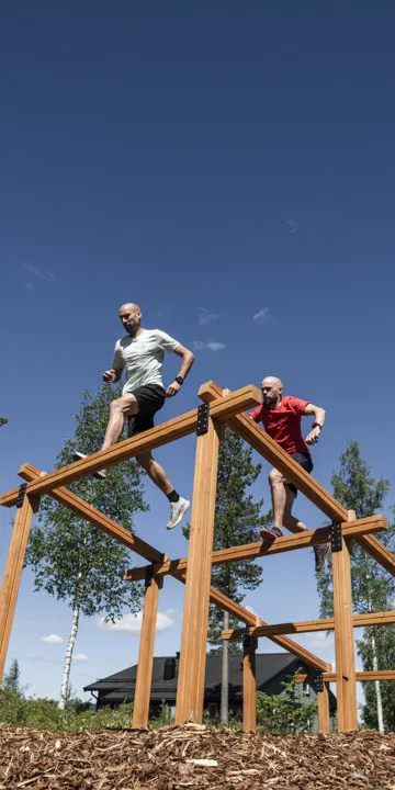 Two people running over one of the high obstacles on Kläppen's obstacle course