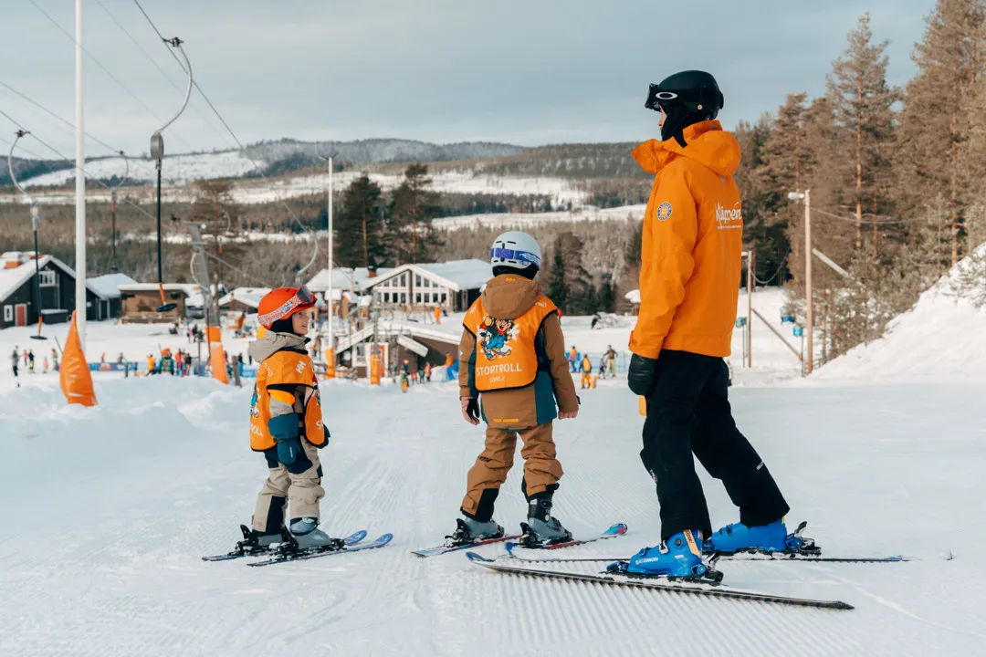 En skidlärare och elev står i skidbacken och skrattar