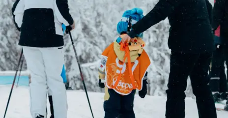 Three skiing girls hold each other's hands as they ski down Lämmeltåget